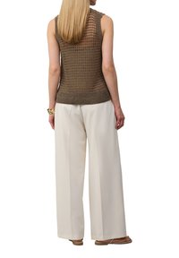 Bruine gebreide mouwloze top met open gaasontwerp, geribbelde zoom, gecombineerd met witte wijde broek en platte sandalen.