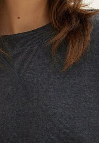 Sudadera gris oscuro con cuello acanalado y tejido de punto texturizado. Presenta un diseño sencillo, textura suave y detalles de costura sutiles.