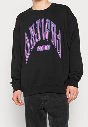 Felpa nera con una vestibilità rilassata, caratterizzata da un audace testo grafico in viola e rosa "ONTWIG 3000." Il materiale sembra morbido, probabilmente una miscela di cotone.