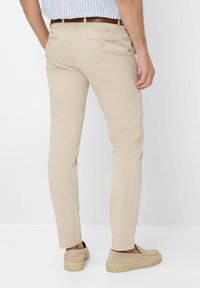 Chino beige con una vestibilità slim, dotati di tasche posteriori con bottoni e una texture liscia, abbinati a scarpe beige slip-on.
