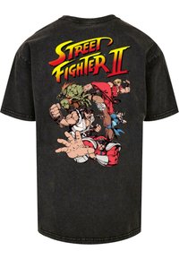 Sort bomulds T-shirt med et levende grafisk print på ryggen, som viser "Street Fighter II" tekst og forskellige karakterer i kamppositioner.