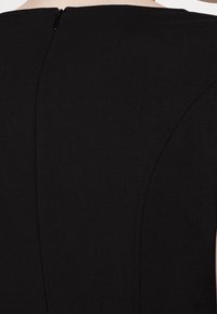 Back of a black dress with visible seam details and a small, centered zipper at the neckline.