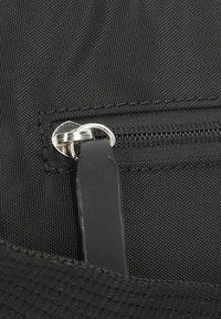 Dettaglio di una borsa in tessuto nero con una cerniera dotata di un tirazip in argento e una superficie testurizzata. L'interno della borsa presenta un rivestimento liscio.