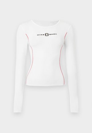 Top branco de manga comprida com costuras laterais vermelhas e decote redondo, apresentando um logótipo preto "NIKE SHOX" no peito. Tecido elástico.