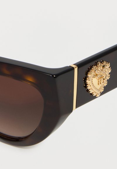 Κοντινή λήψη σκούρων τετραγωνισμένων γυαλιών ηλίου ταρταρούγα με καφέ φακούς και χρυσό διακοσμητικό έμβλημα σε σχήμα καρδιάς στο σκελετό.