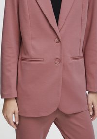 Rosa Blazer mit glatter Textur, mit einer Zwei-Knopf-Verschluss, Reverskragen und seitlichen Taschen. Slim-Fit-Design mit maßgeschneiderten Kanten.