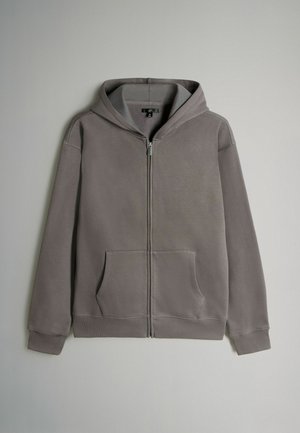 Šedá mikina na zip s přední kapsou, nastavovací kapucí, žebrovanými manžetami a hladkou texturou. Obsahuje jemné švy.