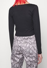 Svart långärmad crop top i kombination med grå byxor med ormskinneprint som har en strukturerad design och figurnära passform. Synliga sömmar och fickdetaljer.