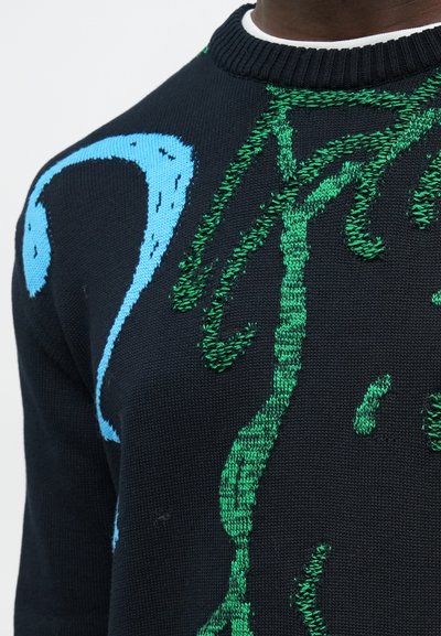 Κοντινή λήψη μαύρου πλεκτού πουλόβερ με αφηρημένα πράσινα και μπλε σχέδια και ριμπ πλεκτή λαιμόκοψη σε άτομο.