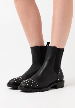 Černé kožené kotníkové boty s texturovanou špičkou zdobenou kovovými nýty. Elastické boční panely a nízká vroubkovaná podrážka pro stabilitu.