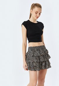 Top corto nero a maniche corte abbinato a una gonna a strati con ruches in stampa leopardata nera e beige. Tessuto leggero con vita elastica.