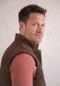 Brown leather vest with a high collar, worn over a ribbed pink sweater. The vest features a front zipper and quilted detailing.