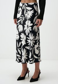 Zwart-witte bloemenprint rok van gladde stof, met een middellange snit en een vloeiende silhouette. Gepaard met zwarte puntige hakken.