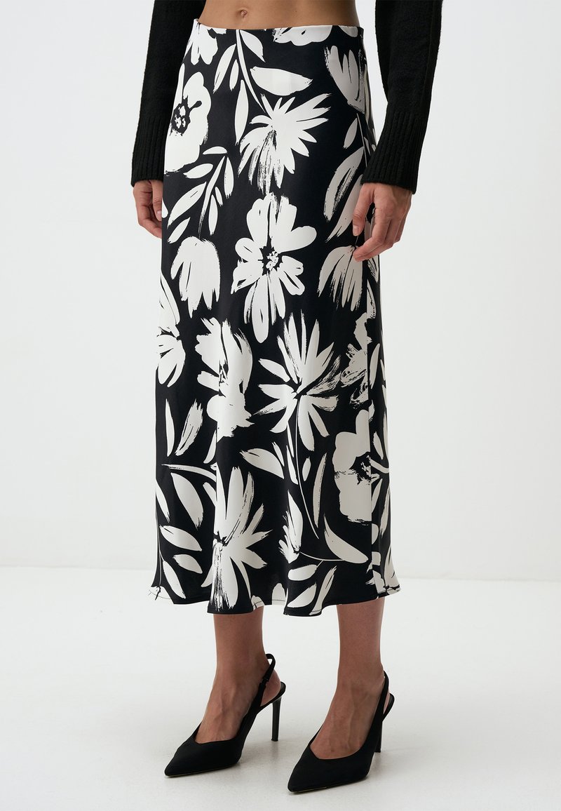 Zwart-witte bloemenprint rok van gladde stof, met een middellange snit en een vloeiende silhouette. Gepaard met zwarte puntige hakken.