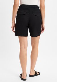 Pantaloni shorts neri in un tessuto leggero, dotati di due tasche posteriori, un cinturino a vita media e un fit rilassato. Tessuto morbido con dettagli di cucitura.