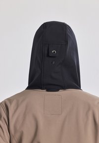 Kapuzenshirt mit einem zweifarbigen Design: schwarze Kapuze mit Knopfdetails und einem beigen Körper mit einer genähten Etikettenfläche auf der Rückseite.
