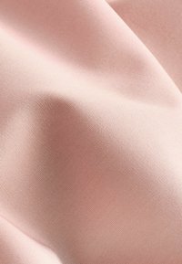 Tela de color rosa claro que presenta una superficie suave y texturizada con un suave brillo. El tejido es apretado y uniforme, lo que resalta su durabilidad.