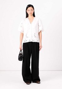 White short-sleeve blouse with perforated design, paired with loose black trousers and leopard-print shoes; holding a small black handbag.