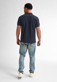 Námořnická polo tričko s límečkem, krátkými rukávy a logem na levém rameni, kombinované se světle modrými džínami s prošoupaným vzhledem a bílými teniskami.