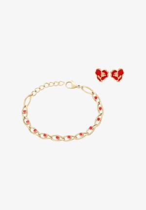 Náramek ze zlatého řetízku s červenými smaltovanými tečkami a náušnice ve tvaru srdce se zlatými a červenými květinovými motivy na bílém pozadí.