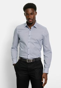 Helles blaues, gemustertes Hemd mit langen Ärmeln und Button-Down-Kragen. Dunkle Knöpfe ergänzen das Design. Kombiniert mit schwarzen Hosen.