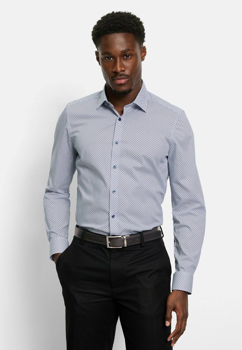 Helles blaues, gemustertes Hemd mit langen Ärmeln und Button-Down-Kragen. Dunkle Knöpfe ergänzen das Design. Kombiniert mit schwarzen Hosen.