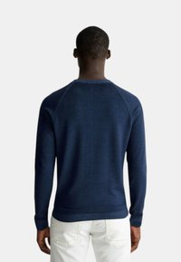 Maglione blu navy con scollo rotondo e maniche lunghe. Texture liscia, polsini e orlo a coste. Presenta un design a manica raglan.