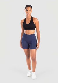 Zwarte sportbeha en marineblauwe shorts met hoge taille van rekbare stof, met een aansluitend ontwerp en een gladde textuur, gecombineerd met witte sneakers.