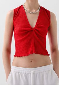 Rød cropped top med et struktureret, krøllet stof. Den har en dyb V-hals og en knude detalje i midten, med en bølget kant.