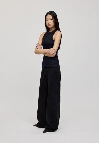 Black sleeveless top paired with wide-leg black pants. The outfit features a smooth texture and a tailored fit, accentuating a minimalist aesthetic.