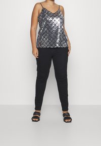 Camiseta sin mangas negra con lentejuelas y escote en V, combinada con pantalones negros ajustados. Footwear con correas texturizadas negras.