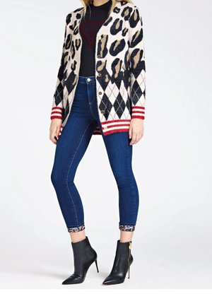 Kardigan w panterkę w czarno-beżowych odcieniach, z czerwonymi, paskowanymi ściągaczami, zestawiony z ciemnymi, obcisłymi dżinsami i czarnymi botkami za kostkę.