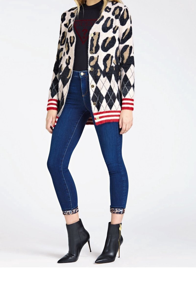 Kardigan w panterkę w czarno-beżowych odcieniach, z czerwonymi, paskowanymi ściągaczami, zestawiony z ciemnymi, obcisłymi dżinsami i czarnymi botkami za kostkę.