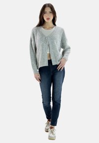 Cardigan lavorato a costine grigio chiaro, con chiusura a nodo, abbinato a jeans skinny blu scuro e sneakers crema. Outfit casual adatto per diverse occasioni.