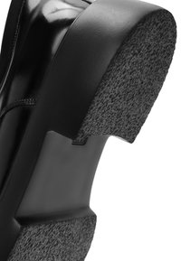 Zwarte hak van een schoen met glanzend, glad leer en een gestructureerde rubberen basis. Heeft een blokvorm en minimale stikseldetails.