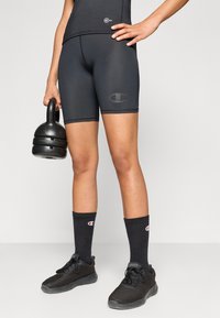 Svarta atletiska shorts i stretchigt material, med en diskret logotypdetalj. Matcher med svarta träningsstrumpor och skor, håller i en kettlebell.