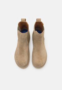 Botas de ante beige hasta el tobillo con paneles laterales elásticos y una tira de agarre. El diseño elegante cuenta con una puntera redondeada y una suela intermedia texturizada para mayor agarre.