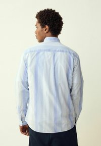 Mėlynos ir baltos juostelės marškiniai su ilgomis rankovėmis, su tradiciniu apykakle ir išlenktu kraštu, pagaminti iš lengvos medžiagos.