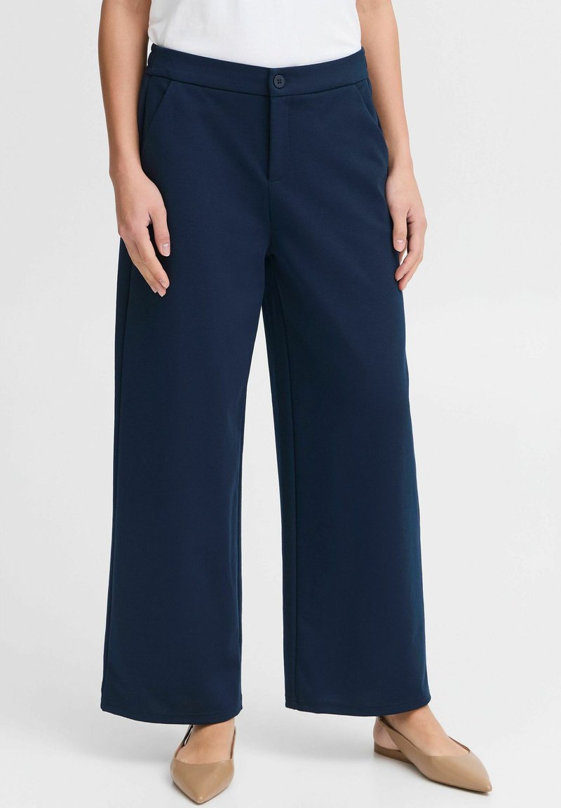 Pantaloni a gamba larga blu navy realizzati in un tessuto morbido e liscio, con vita con bottone e tasche laterali; indossati con ballerine beige a punta.