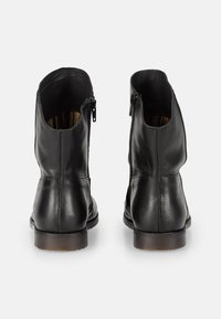 Botas de tobillo de cuero negro con una textura suave, cuentan con una cremallera lateral y un forro interno de rayas contrastantes. Diseño minimalista y suela robusta.