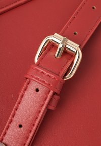 Cinturino in pelle rossa con dettaglio in metallo dorato. Presenta una superficie texturizzata, cuciture e diversi fori di regolazione per personalizzare la misura.
