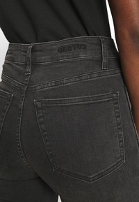 Jeans neri a vita alta con vestibilità aderente, caratterizzati da cuciture sottili e un logo sulla cintura, e un classico design a cinque tasche.