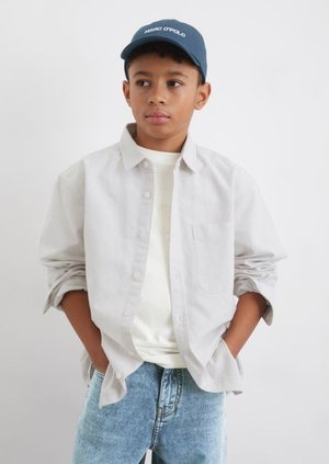 Gestreiftes Button-Down-Hemd in Hellgrau, über einem weißen T-Shirt getragen, kombiniert mit hellblauen Jeans, Baseballmütze in Dunkelblau mit flachem Schirm.