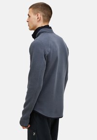 Man wearing a gray textured fleece jacket and black pants, facing left with a neutral background.