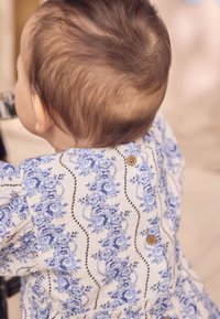 Fehér, kék rózsákkal díszített virágmintás ruha, texturált kialakítással és apró fa gombokkal a hátoldalon. Puha, könnyű anyagból.