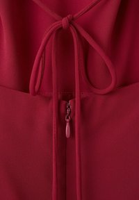 Približek temno rdeče tkanine z zavezanim lokom nad zaprtim zadrgo z ujemajočim se jezičkom za poteg.