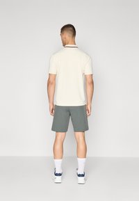 Ανδρικό κρεμ πόλο πουκάμισο με σκούρο γιακά, σε συνδυασμό με πράσινες βερμούδες. Τα λευκά κάλτσες και τα αθλητικά παπούτσια ολοκληρώνου�ν την εμφάνιση. Μινιμαλιστικός σχεδιασμός και χρώματα.