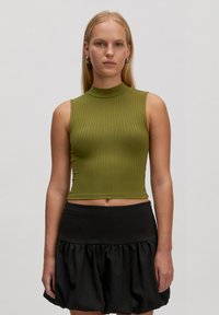 Olijfgroen geribde crop top met een hoge halslijn en mouwloos design, gecombineerd met een zwarte rok met ruches. Vriendelijke, gladde textuur.