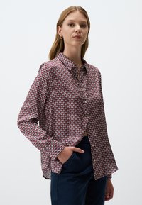 Bedrucktes Hemd mit Knöpfen aus einem leichten Stoff, das ein geometrisches Muster in Rot, Blau und Weiß aufweist, mit einem Kragen und langen Ärmeln.
