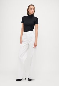 Top de cuello alto negro con relieve, combinado con pantalones blancos de pernera ancha. Zapatos de tacón alto negros completan el conjunto.